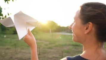 vrouw lanceert papier vliegtuig tegen zonsondergang achtergrond. concept van dromen over op reis of de beroep van een stewardess. video