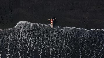 parte superior ver de un niña en un rojo traje de baño acostado en un negro playa en el navegar línea. costa de el isla de tenerife, canario video