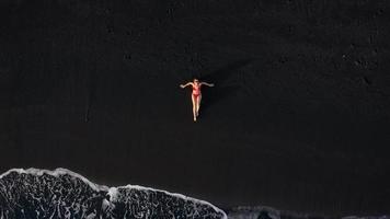 topp se av en flicka i en röd baddräkt liggande på en svart strand på de surfa linje. kust av de ö av teneriffa, kanariefågel video