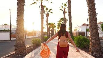 Happy woman in a big yellow hat walking along a palm alley at sunset video