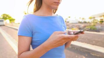 Woman in a blue dress using smartphone while walks on a palm street at sunset video