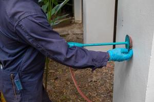 exterminate termite control company employee is using a termite sprayer at customer's house and searching for termite nests to eliminate. exterminate control worker spraying chemical insect repellant photo