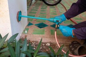 exterminate termite control company employee is using a termite sprayer at customer's house and searching for termite nests to eliminate. exterminate control worker spraying chemical insect repellant photo