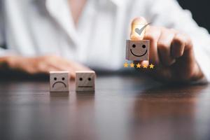 Customer service evaluation and satisfaction survey concepts. The client's hand picked the happy face smile face icon and five star symbol on wooden cube on table photo