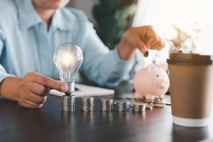 Businesswoman hand holding lightbulb and putting coin in piggy bank. Idea of saving energy and accounting finance in home and family, save world and energy power. Save energy plan concept photo