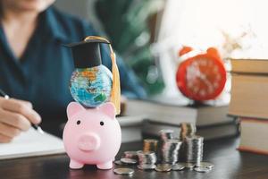 Graduation cap with globe on pink piggy bank with stack of coins. Concept of saving money for scholarship to study abroad at university level. Financial planning accounting ideas for future education. photo