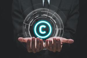 Copyright or patent concept, Business person hand holding VR screen copyright icon with blue bokeh background, Copyleft trademark license, Creation ownership against piracy crime. photo