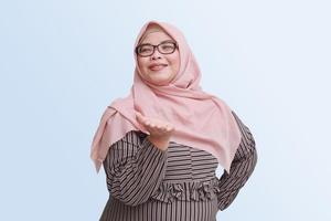 Portrait of cheerful Asian woman with hijab, showing something on empty hand. Advertising concept. Isolated image on pink background photo