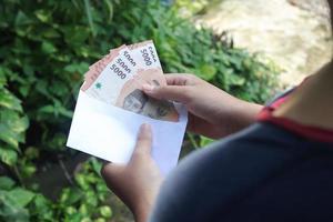 Close up of male hand inserting five thousand rupiah money banknote into envelope. Financial and savings concept photo