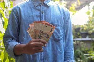 Close up of male hand holding five thousand rupiah money banknote. Financial and savings concept photo