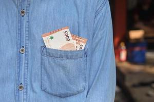 Close up of five thousand rupiah money banknote inside of shirt pocket. Financial and savings concept photo