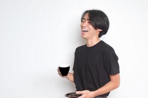 Portrait of excited Asian man in black t-shirt laughing out loud while holding a saucer and a coffee cup. Isolated image on white background photo