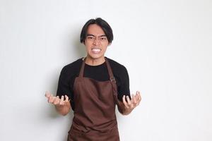 Portrait of annoyed Asian barista man in brown apron making angry hand gesture with fingers. Isolated image on white background photo