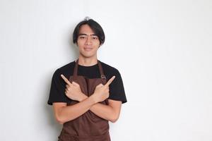 Portrait of attractive Asian barista man in brown apron showing product, pointing up right and left, showing two option of choices. Advertising concept. Isolated image on white background photo