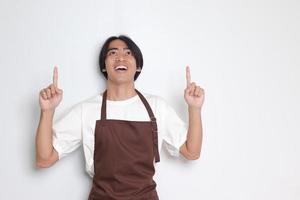 Portrait of attractive Asian barista man in brown apron showing product, pointing at something with hands. Advertising concept. Isolated image on white background photo