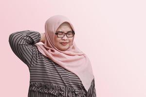 Portrait of cheerful Asian woman with hijab, having a migraine, touching her temple. Healthcare concept. Isolated image on pink background photo