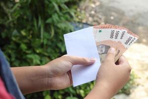 cerca arriba de masculino mano insertando cinco mil rupia dinero billete de banco dentro sobre. financiero y ahorros concepto foto