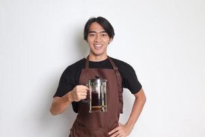 retrato de atractivo asiático barista hombre en marrón delantal señalando con dedo y demostración francés prensa café fabricante. aislado imagen en blanco antecedentes foto