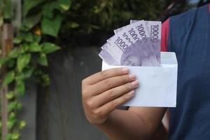 Close up of male hand inserting ten thousand rupiah money banknote into envelope. Financial and savings concept photo