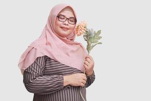 Portrait of happy Asian woman with hijab, holding peach roses flower. Isolated image on gray background photo