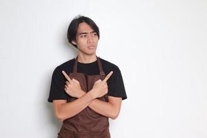 Portrait of attractive Asian barista man in brown apron showing product, pointing up right and left, showing two option of choices. Advertising concept. Isolated image on white background photo