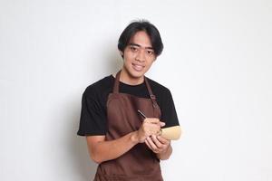 Portrait of attractive Asian barista man in brown apron taking order, writing on menu book list. Isolated image on white background photo