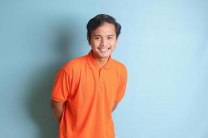 atractivo asiático hombre en naranja camisa mirando a cámara y sensación seguro. aislado imagen en azul antecedentes foto