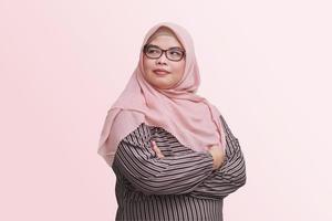 Portrait of confident Asian businesswoman with hijab, keeping arms crossed and looking away. Isolated image on pink background photo