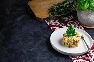 Salad with red fish, Olivier, in a white bowl on the black table photo