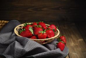 mimbre cesta con dulce rojo fresas en un oscuro de madera mesa. foto