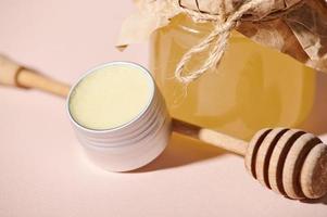 Jar with wax, wooden honey spoon against beige pastel background. Natural cosmetic products made from organic honey photo