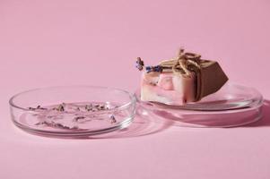 Details on a bar of pink marble soap on petri dish with dry lavender flowers over isolated pink background.Skin care photo