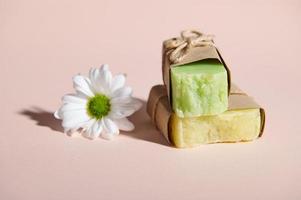 Still life with handmade organic cold pressed soap bars with natural ingredients and chamomile flower on pink background photo