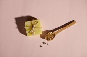 View from above of gelatin capsules in wooden spoon and soap bar tied with linen rope on isolated pink pastel background photo