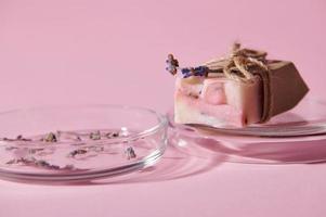Focus on a bar of pink soap with natural ingredients, on petri dish, isolated over pink background. Hygiene. Purity photo