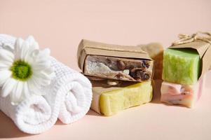 Still life with spa set white rolled towels and organic homemade cold-pressed soap bars, isolated on pink background photo