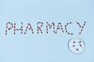 The word PHARMACY laid out on blue background next to Petri dish with medical capsules. Copy space. World Pharmacist Day photo