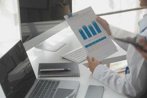 Asian Businesswoman Using laptop computer and working at office with calculator document on desk, doing planning analyzing the financial report, business plan investment, finance analysis concept. photo