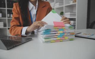 Asian Businesswoman Using laptop computer and working at office with calculator document on desk, doing planning analyzing the financial report, business plan investment, finance analysis concept. photo