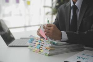 Asian Businesswoman Using laptop computer and working at office with calculator document on desk, doing planning analyzing the financial report, business plan investment, finance analysis concept. photo