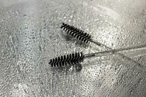 Two black cosmetic brushes for eyebrows and eyelashes lie on a wet table photo