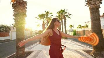 gelukkig vrouw in een groot geel hoed wandelen langs een palm steeg Bij zonsondergang video