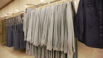 Clothes lined up on shelves in clothing store, shirts and dresses sold in clothing stores are hung on hangers, selective focus video