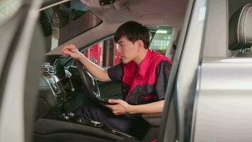 un Jeune expert asiatique Masculin automobile mécanicien technicien vérification une entretien liste avec tablette dans voiture intérieur à garage. véhicule un service réparer et réparation travaux, industriel Occupation affaires emplois. video