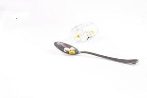 glass container and a silver spoon with medicine on a white isolated background photo