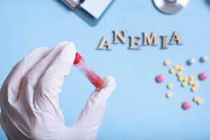 Container with blood analysis in gloved hand and anemia text with cstethoscope, pills photo