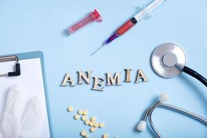 Anemia text with container for blood analysis, stethoscope, pills, syringe flat lay, top view photo