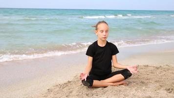 niña lo hace yoga en el playa. adolescente es sentado en el loto posición. video