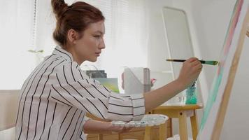 garota artista feminina profissional usa pincel em arte abstrata para criar obra-prima. pintura de pintor com aquarelas ou óleo na casa do estúdio. mulher bonita gosta de pintar como hobby. recreação de trabalho video