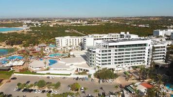 Ayia Napa, Cyprus - 15th april, 2023 - Luxury hotel buildings with pools by beach with island greenery panorama. Vehicles in Nissi bay parking. video